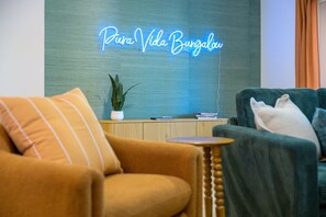 A living room with a neon sign reading 'Pura Vida Bungalow,' a plant on a wooden side table, and two armchairs with cushions. - Poolside Oasis Sleeps 8 Game Room Putt Putt (Bradenton)