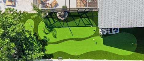 Vista aérea de una propiedad con piscina, un patio cubierto y un césped cuidado con diseño de campo de golf.