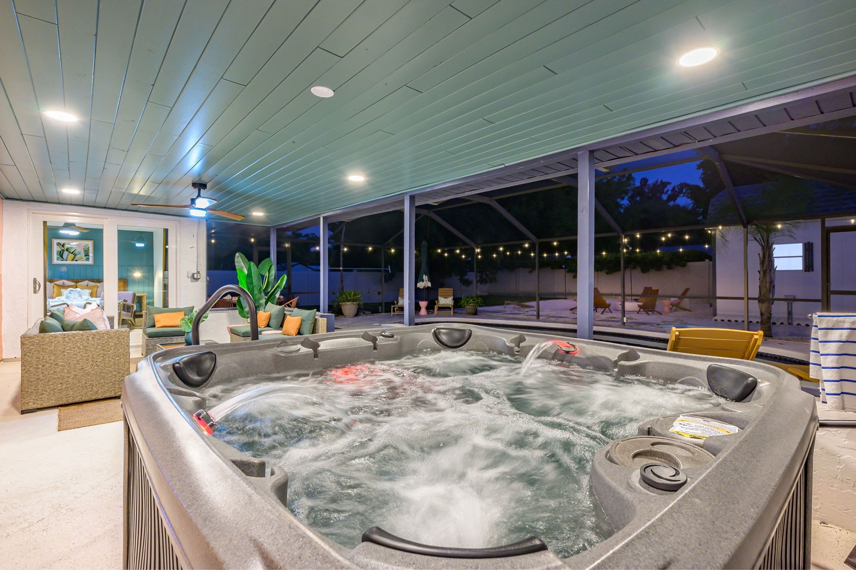 A hot tub with a view of the outdoors, a seating area with cushions, and a ceiling with recessed lighting.