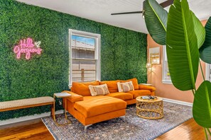A room with a green wall, a neon sign, a sofa, a bench, and a large plant. - Sunny Citrus Escape Min to Midtown Dog-friendly (Tampa)