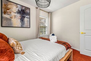 A bedroom with a bed, pillows, a window with blinds, a door, and a wall-mounted artwork. - Sunny Citrus Escape Min to Midtown Dog-friendly (Tampa)