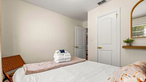 Un dormitorio con cama, una silla, una puerta y una planta pequeña.