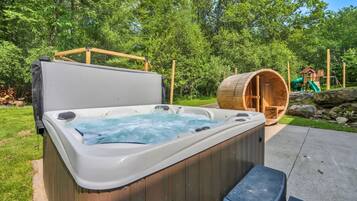 A hot tub with a wooden exterior, a wooden deck, and a play structure in the background.