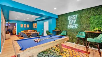 A pool table with a colorful mosaic floor, a green wall with a 'BEST DAY EVER' sign, and a billiards setup.