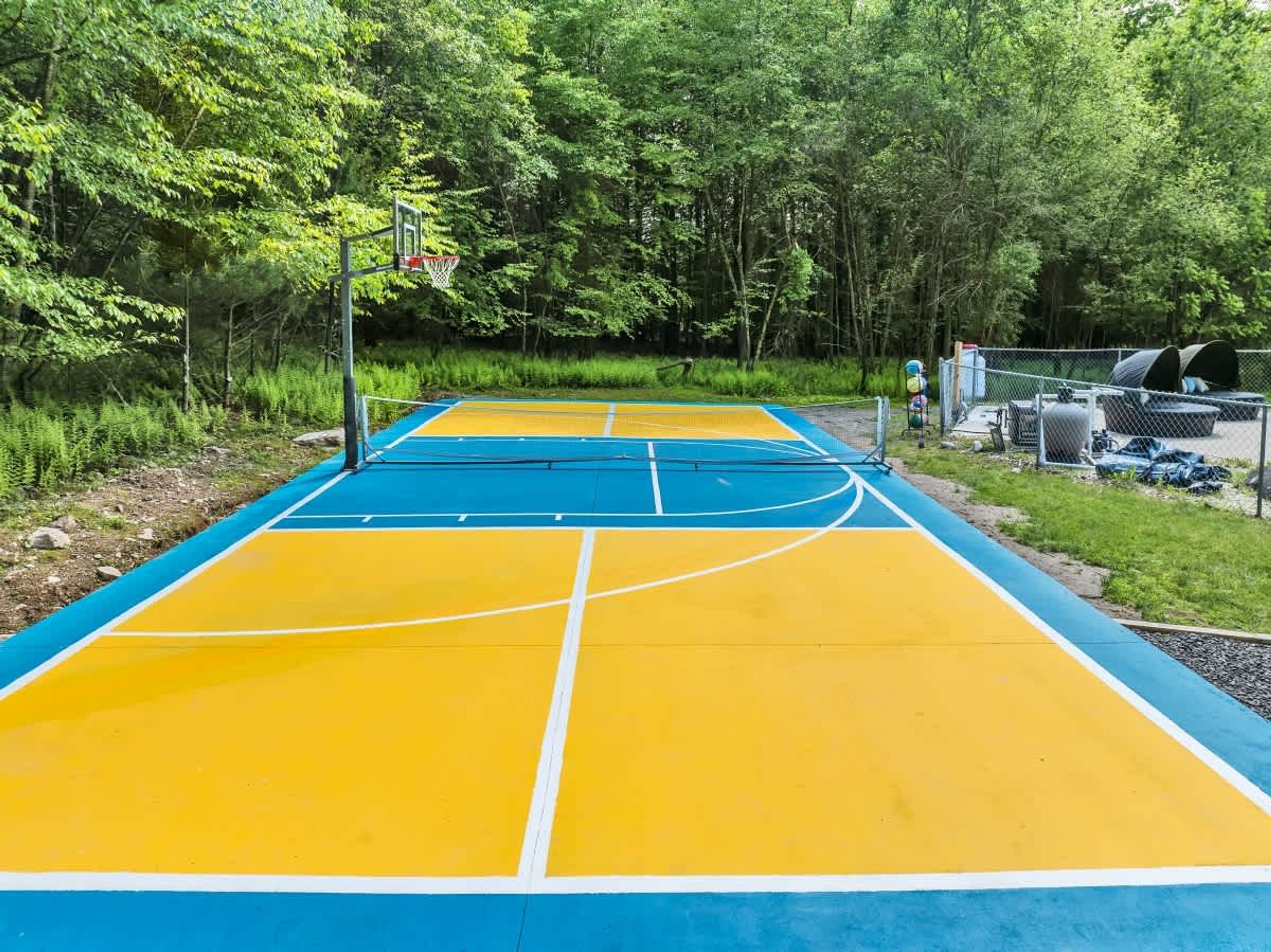 Una cancha de baloncesto al aire libre con superficie azul y amarilla, rodeada de árboles.