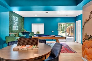 Une pièce avec une table de billard, des chaises, un néon et une vue sur l’extérieur.