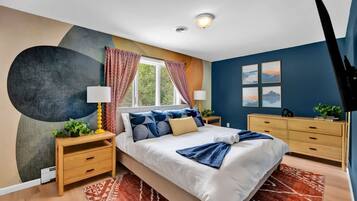 A modern bedroom with a large bed, bedside tables, a window with curtains, a wall-mounted lamp, and a painting.