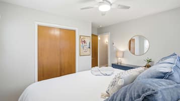 A bedroom with a bed, a ceiling fan, a door, a mirror, and a nightstand.