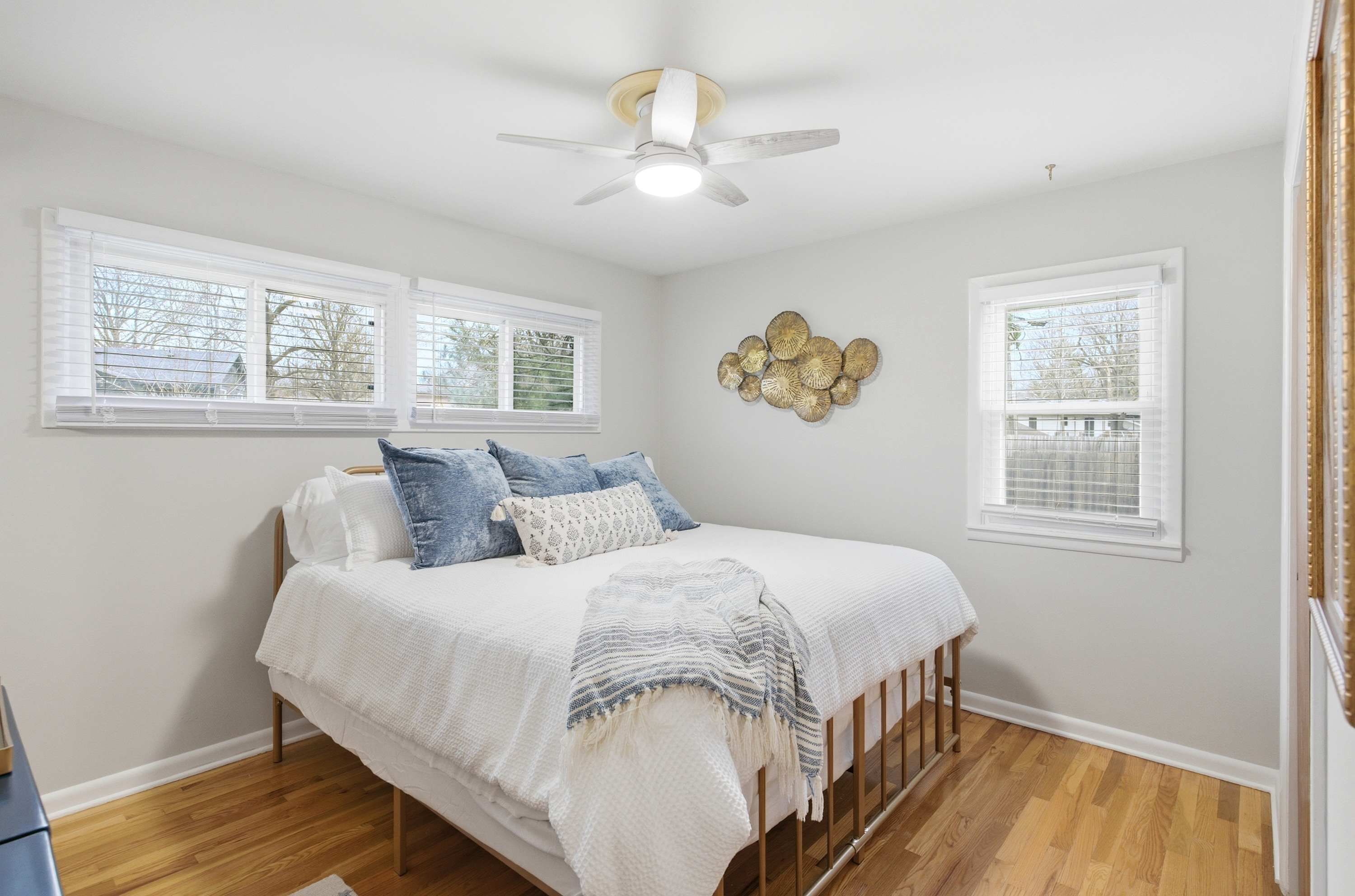 A bedroom with a bed, a ceiling fan, and two windows with blinds.