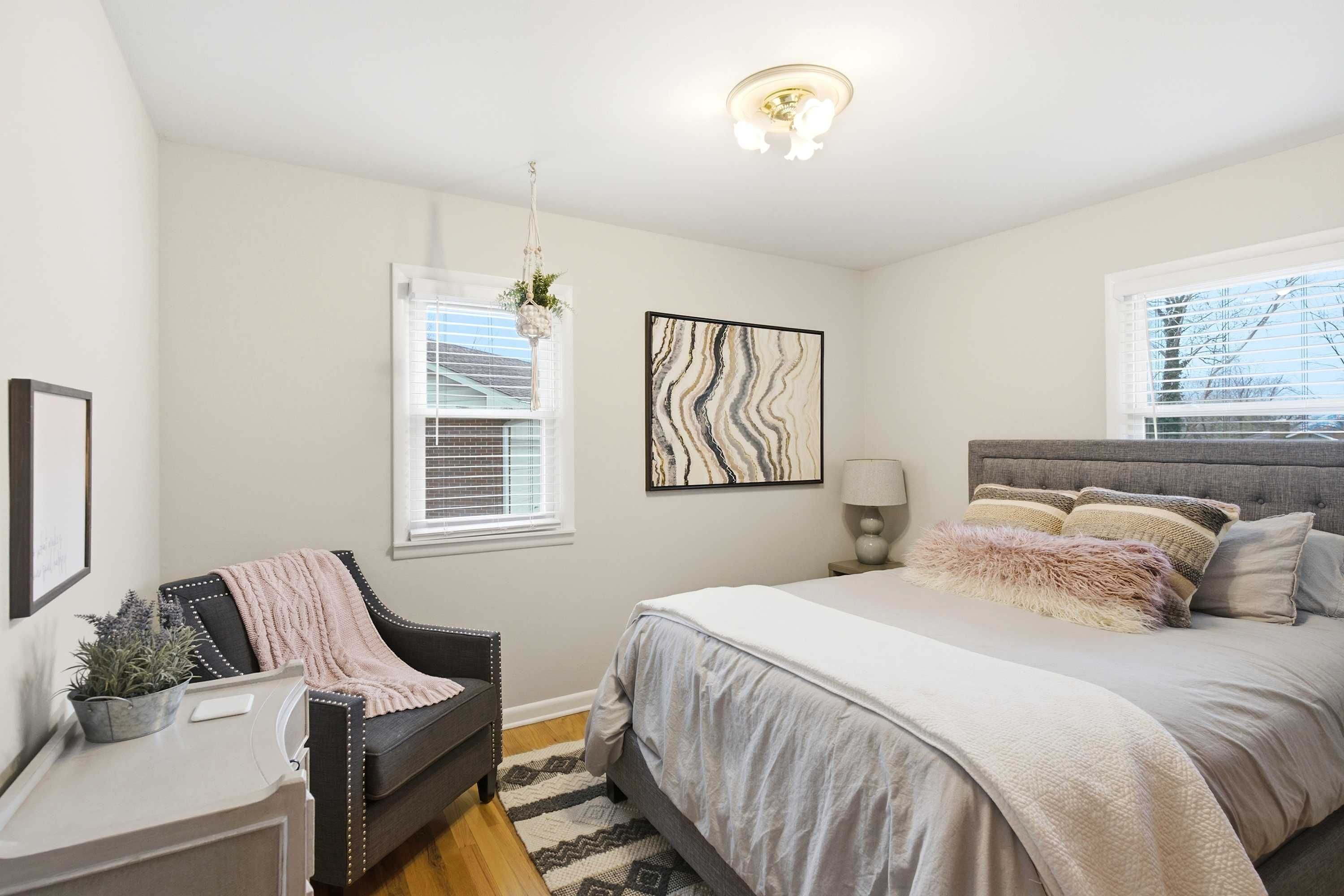 A bedroom with a bed, a chair, a desk, a window, and a wall-mounted artwork.