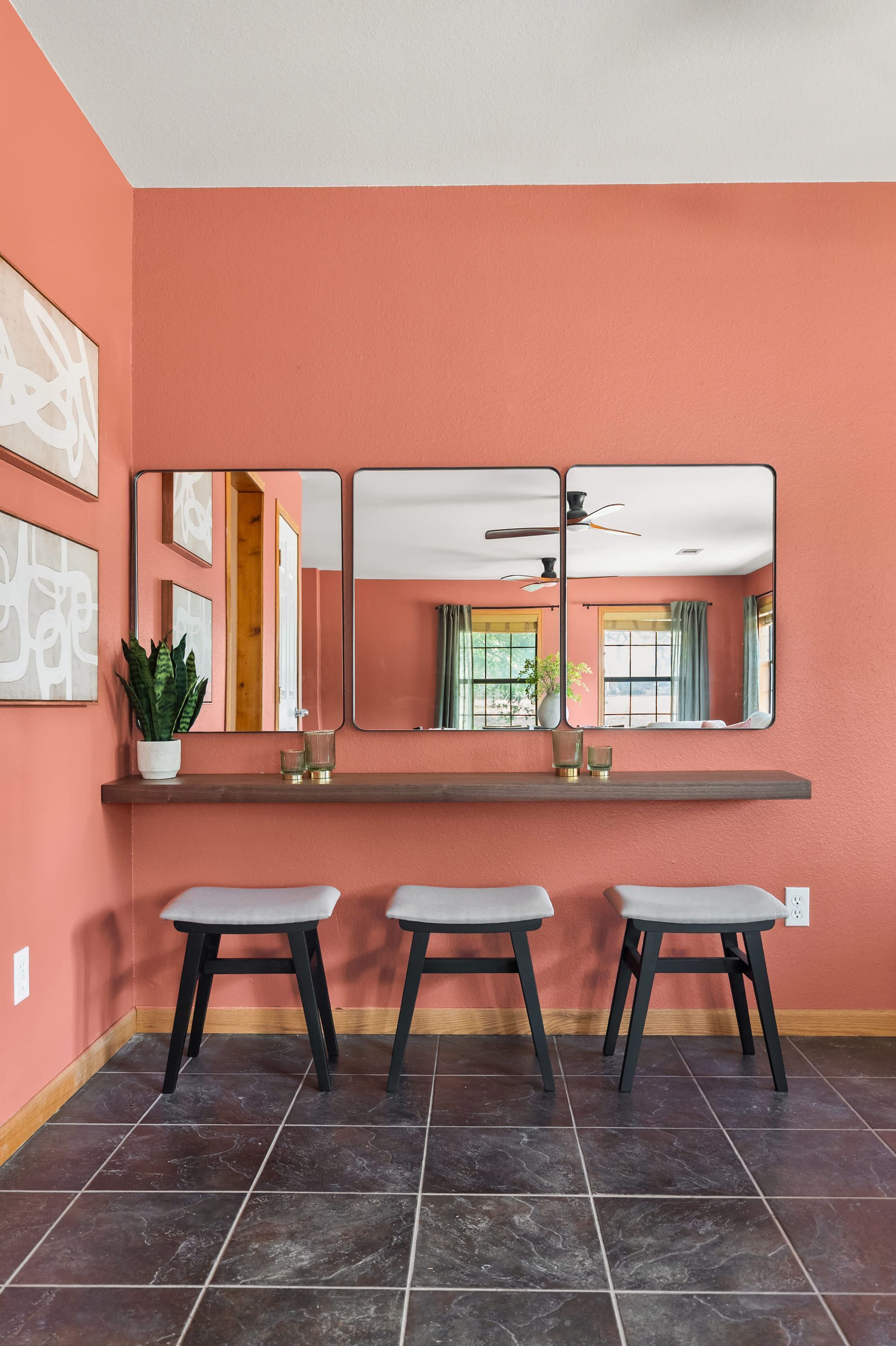 A room with a large mirror, two stools, a potted plant, and a window with curtains.
