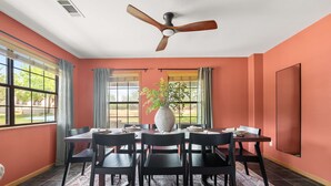 A dining room with a table set for four, a ceiling fan, and large windows with curtains. - Birdie Creek Ranch - Private Golf Course Resort (Driftwood)
