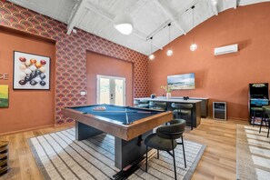 Ein Billardtisch in einem Raum mit strukturiertem Wandpapier, einer Bar und einem Fernseher.