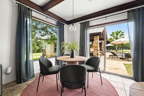 A room with a round table and four chairs, large windows with curtains, a hanging light fixture, and a view of an outdoor patio with a stone fireplace. - Birdie Creek Ranch - Private Golf Course Resort (Driftwood)