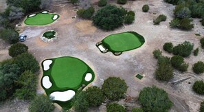 Luftaufnahme eines Golfplatzes mit mehreren Grüns, Sandbunkern und vereinzelten Bäumen.