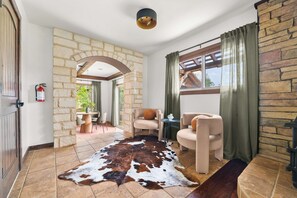 Una habitación con pared de piedra, alfombra de cuero de vaca y una ventana con cortinas.