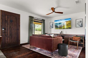 A room with a wooden door, a ceiling fan, a sofa, a chair, a desk, and artwork on the wall. - Birdie Creek Ranch - Private Golf Course Resort (Driftwood)