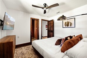 A bedroom with a bed, a desk, a ceiling fan, a mounted picture, and a door leading to another room. - Birdie Creek Ranch - Private Golf Course Resort (Driftwood)