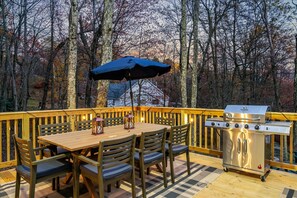 Eine Terrass mit Holztisch und -stühlen, einem Grill und einem blauen Sonnenschirm.