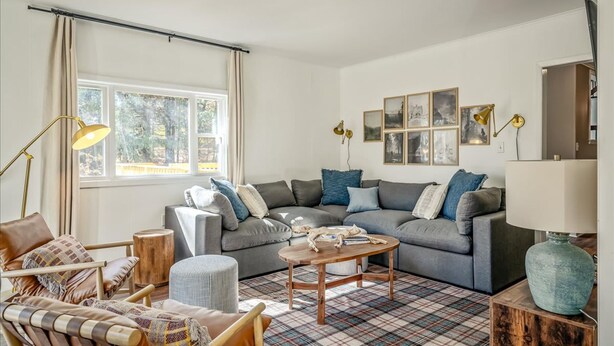 En stue med en grå sofa, et træbord, et ternet tæppe og et vindue med gardiner.