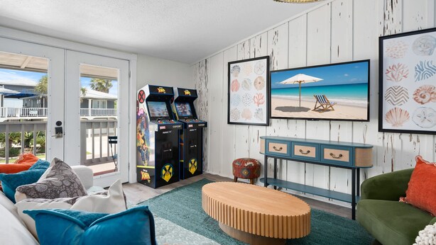 Una stanza con un divano, un tavolino, giochi arcade, un quadro a tema spiaggia e vista sull'esterno.