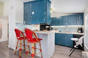 Uma cozinha com armários azuis, uma ilha branca, duas cadeiras vermelhas e uma mesa branca.