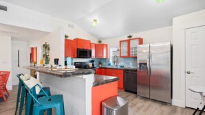 Una cucina moderna con mobili rossi, un frigorifero in acciaio inossidabile e un angolo bar con sgabelli.