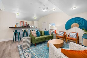 Ein Wohnzimmer mit einem grünen Sofa, gemusterten Kissen, einem runden Couchtisch und einem blau karierten Teppich.