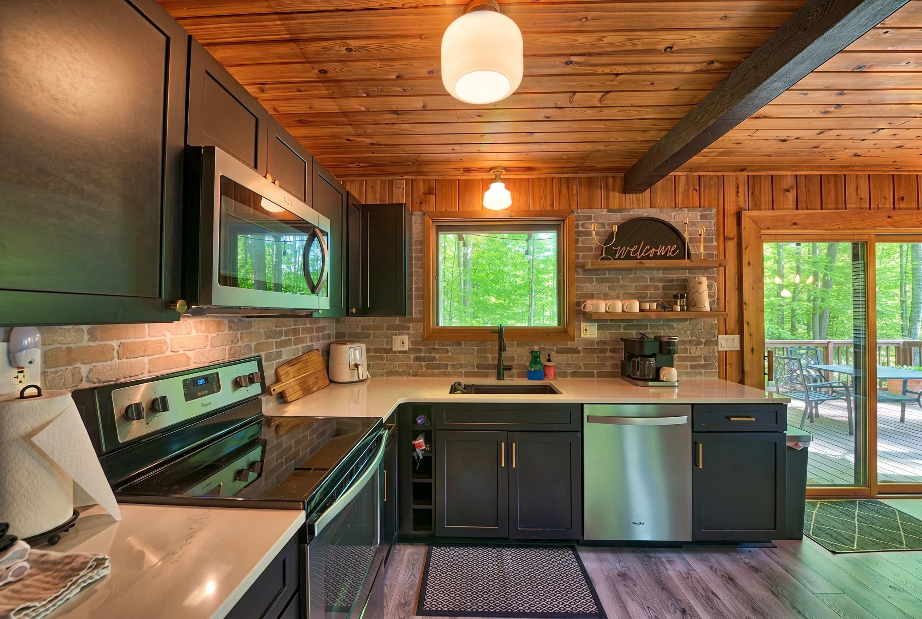Cocina moderna con horno integrado, un lavamanos y ventana con vistas a un bosque.