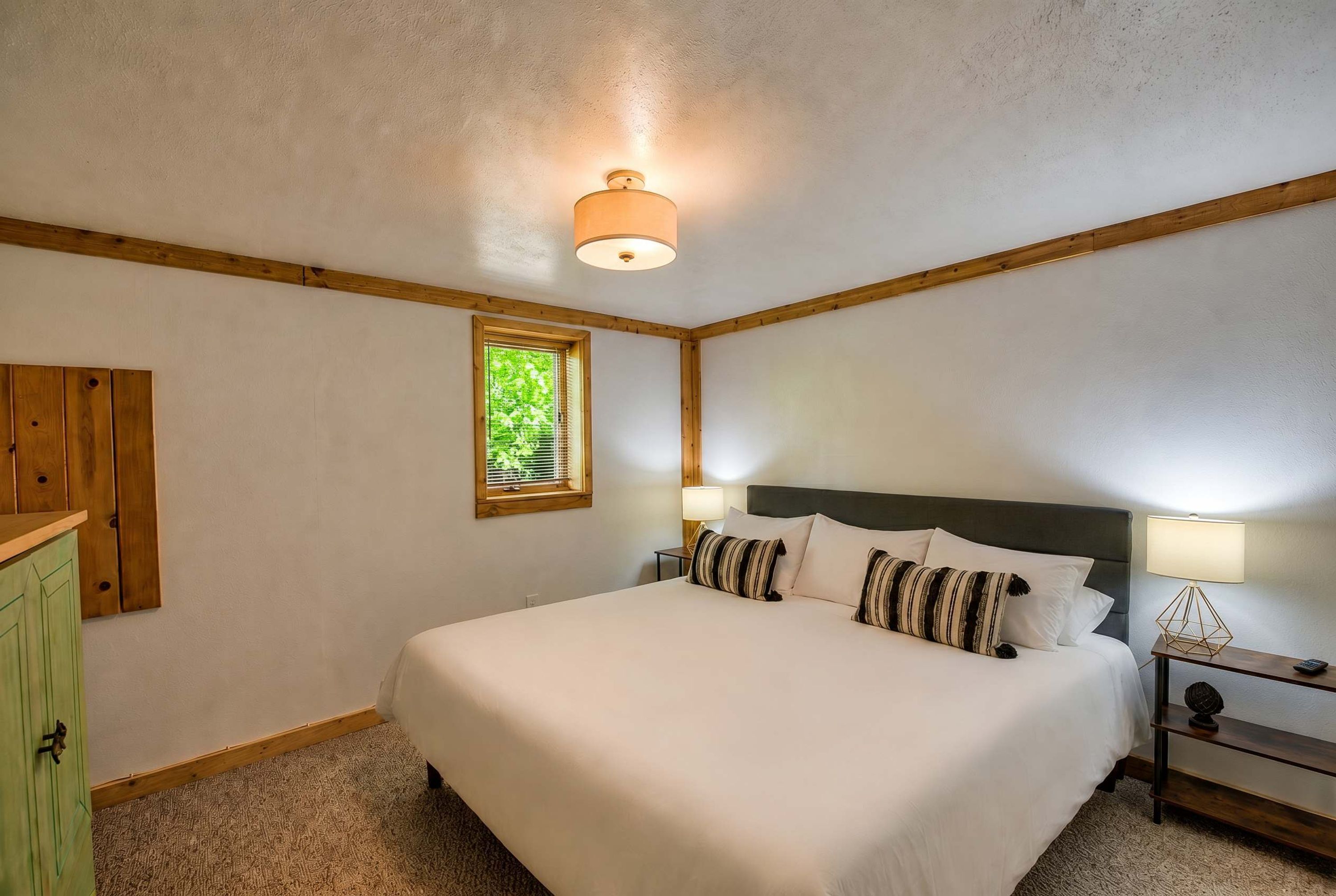 A bedroom with a large bed, a nightstand, a lamp, a window, and a wooden headboard.