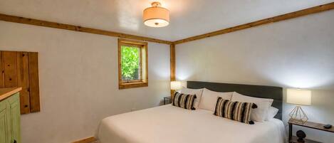 A bedroom with a large bed, a nightstand, a lamp, a window, and a wooden headboard.