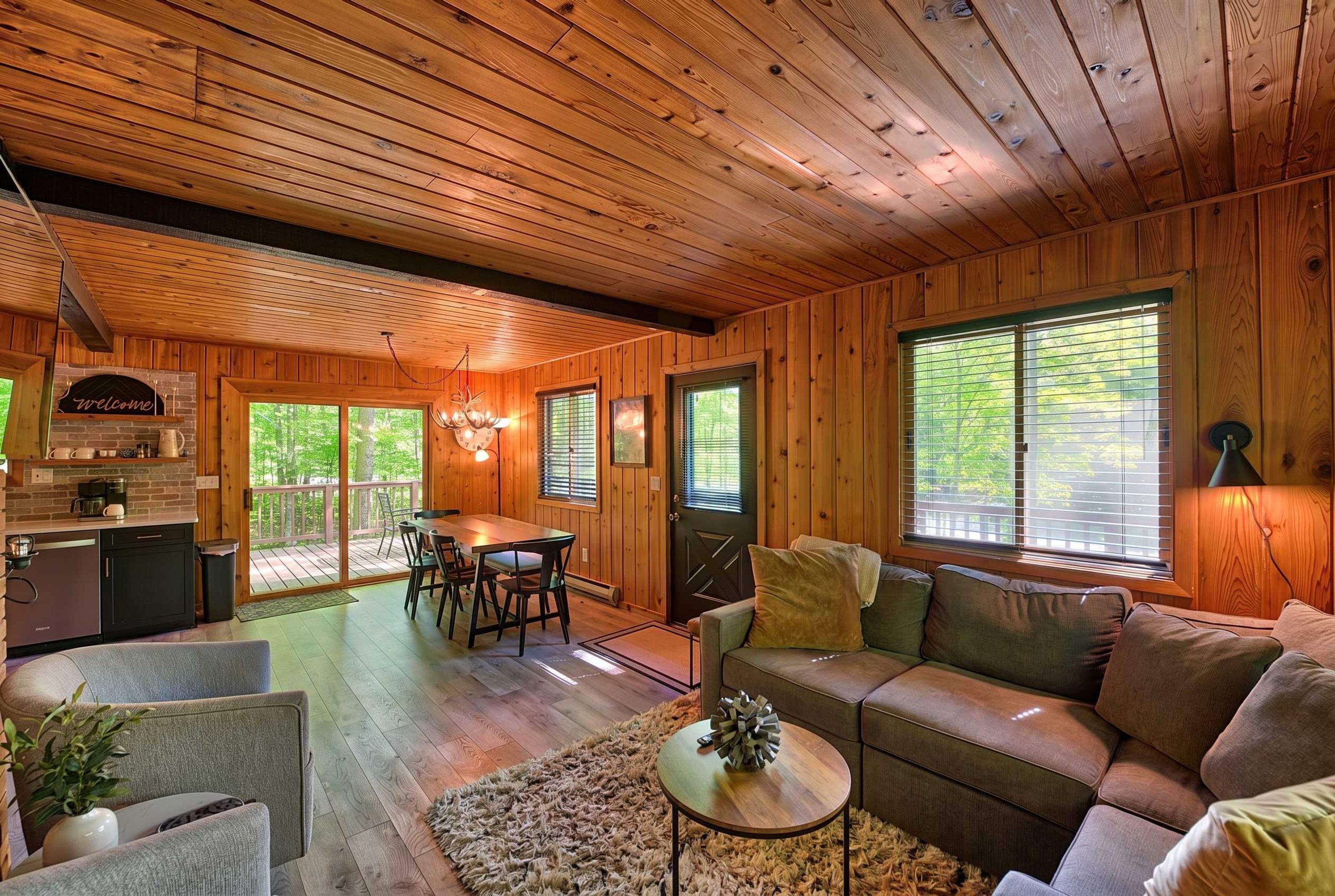 A wooden cabin interior with a dining area, sofa, and a fireplace.