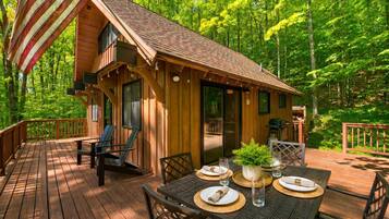 A wooden cabin with a deck, outdoor seating, and a dining table set for two.