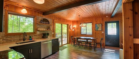 A wooden interior with a kitchen, dining area, and a door leading outside.