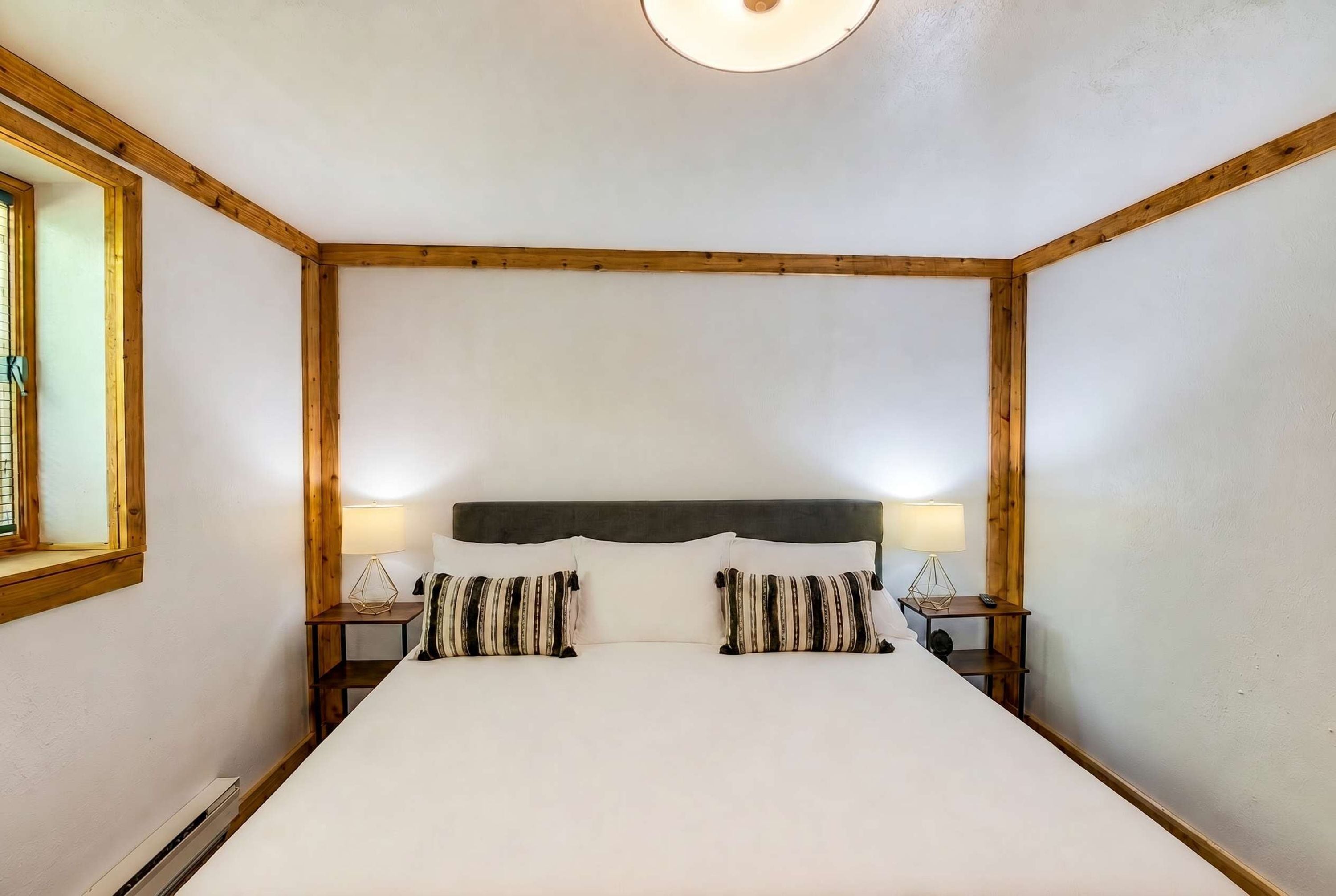 Una habitación con una cama grande, cabecera de madera, dos mesitas de noche con lámparas y una ventana con persianas.