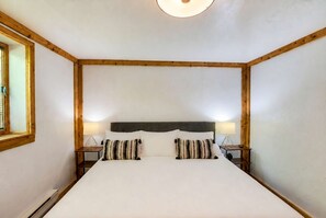 Una habitación con una cama grande, cabecera de madera, dos mesitas de noche con lámparas y una ventana con persianas.