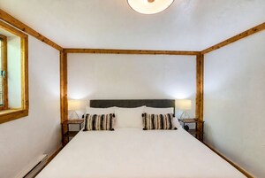 A room with a large bed, wooden headboard, two bedside tables with lamps, and a window with blinds.