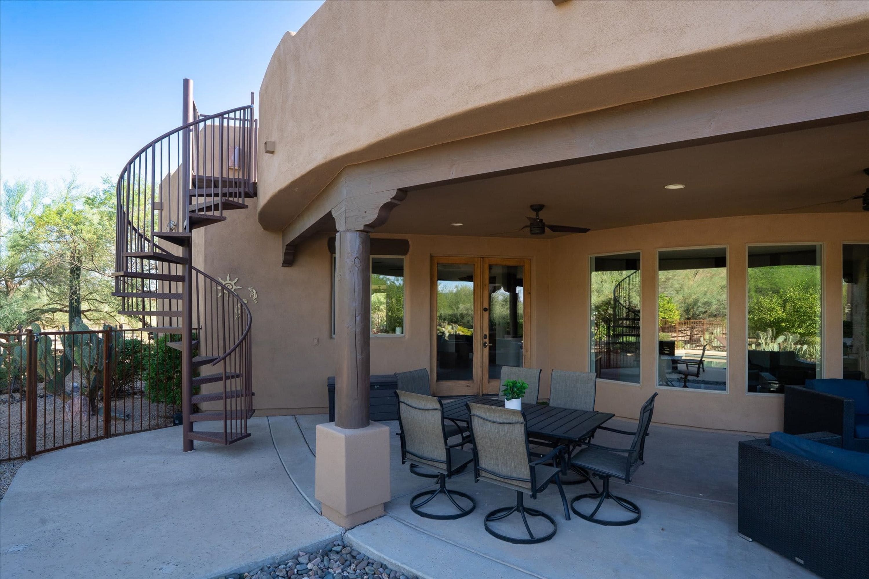 A covered patio with outdoor furniture, a spiral staircase, and large windows.
