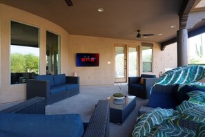 Ein moderner Außenbereich mit blauen Sofas, einem Flachbildfernseher, der das Netflix-Logo zeigt, und einem Deckenventilator.