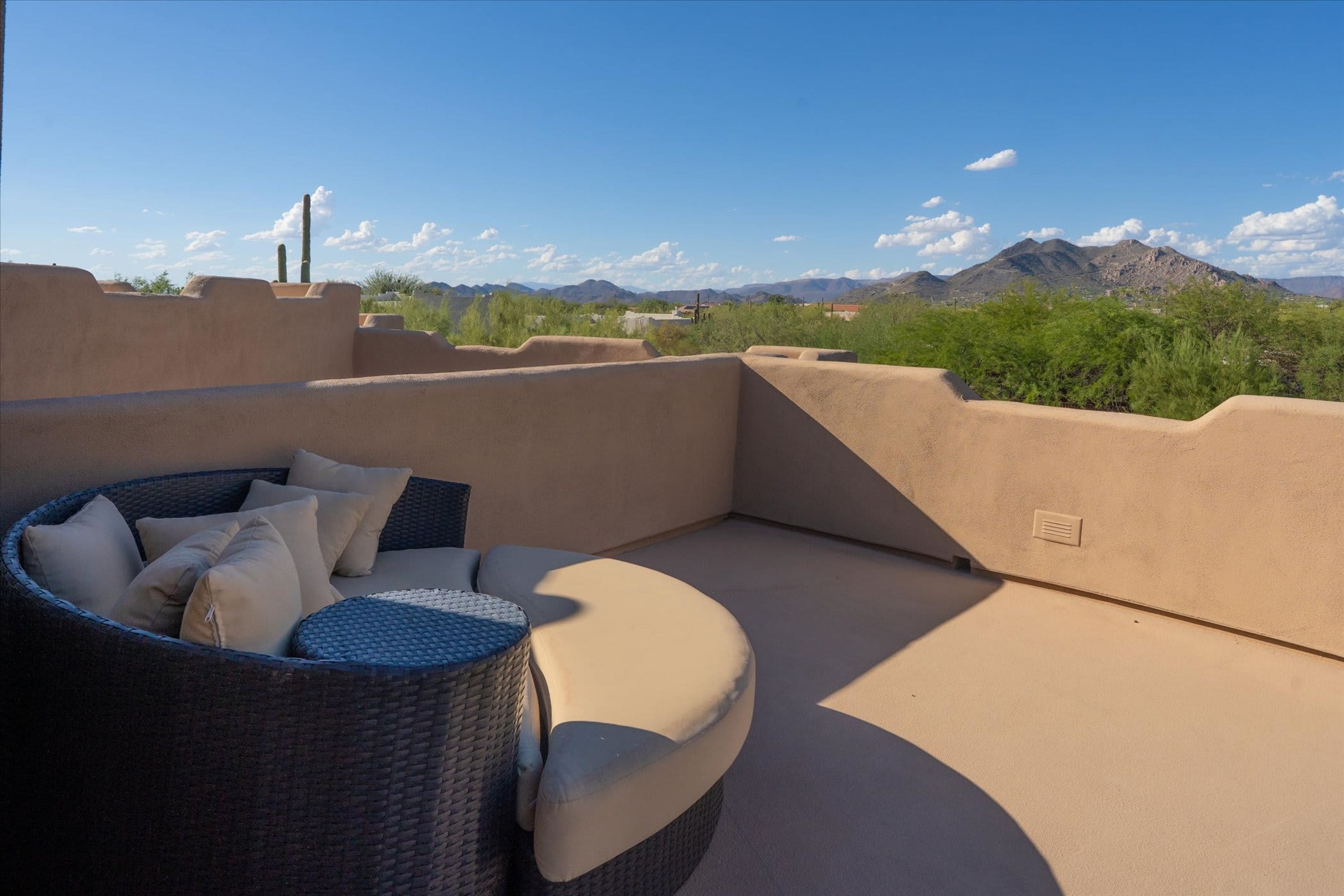 A rooftop patio with a curved sofa and cushions, overlooking a mountainous landscape.