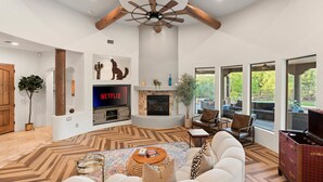 Una sala de estar moderna con chimenea, ventilador de techo y un amplio ventanal con vistas al exterior.