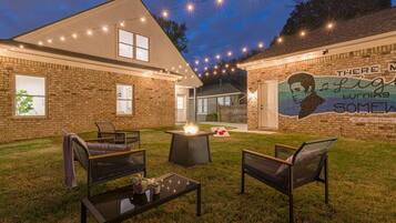 A backyard with a brick house, outdoor seating, a fire pit, and string lights.