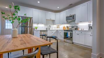A modern kitchen with white cabinetry, stainless steel appliances, and a wooden dining table.