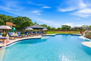Ein Swimmingpool mit Liegestühlen und Sonnenschirmen, umgeben von einer Holzterrasse und einem Baseballfeld.