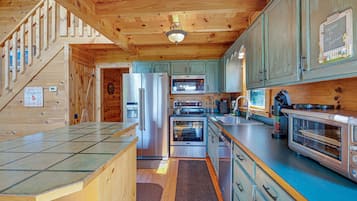 A wooden cabin kitchen with a refrigerator, oven, microwave, and a coffee machine.