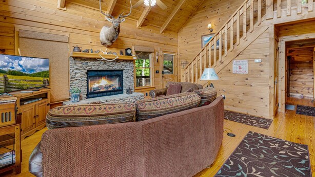 A cozy cabin interior with a stone fireplace, a ceiling fan, and a mounted deer head. - Mountain Views w Slide Hot Tub Game Room (Mineral Bluff)