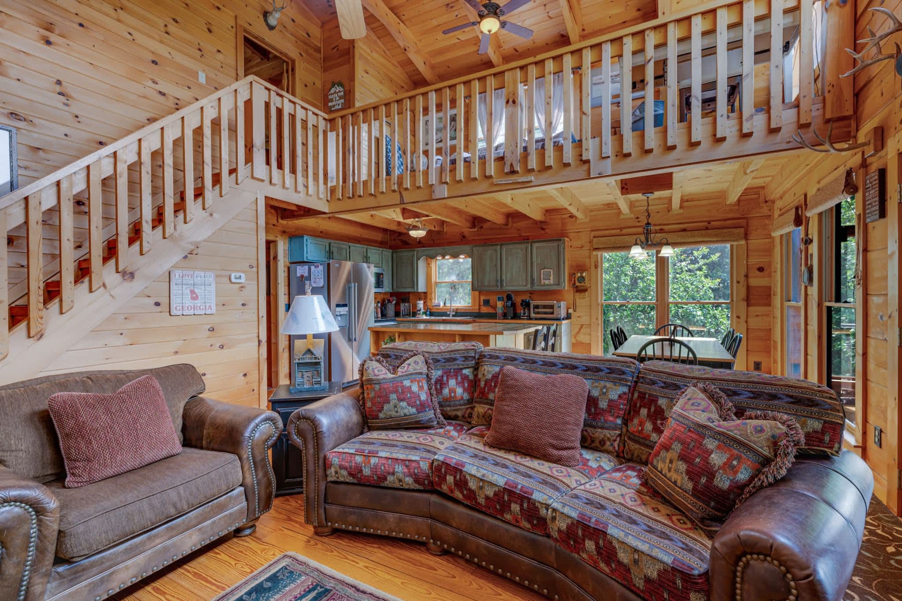 A wooden cabin interior with a staircase, a sofa, a dining table, and a kitchen area.