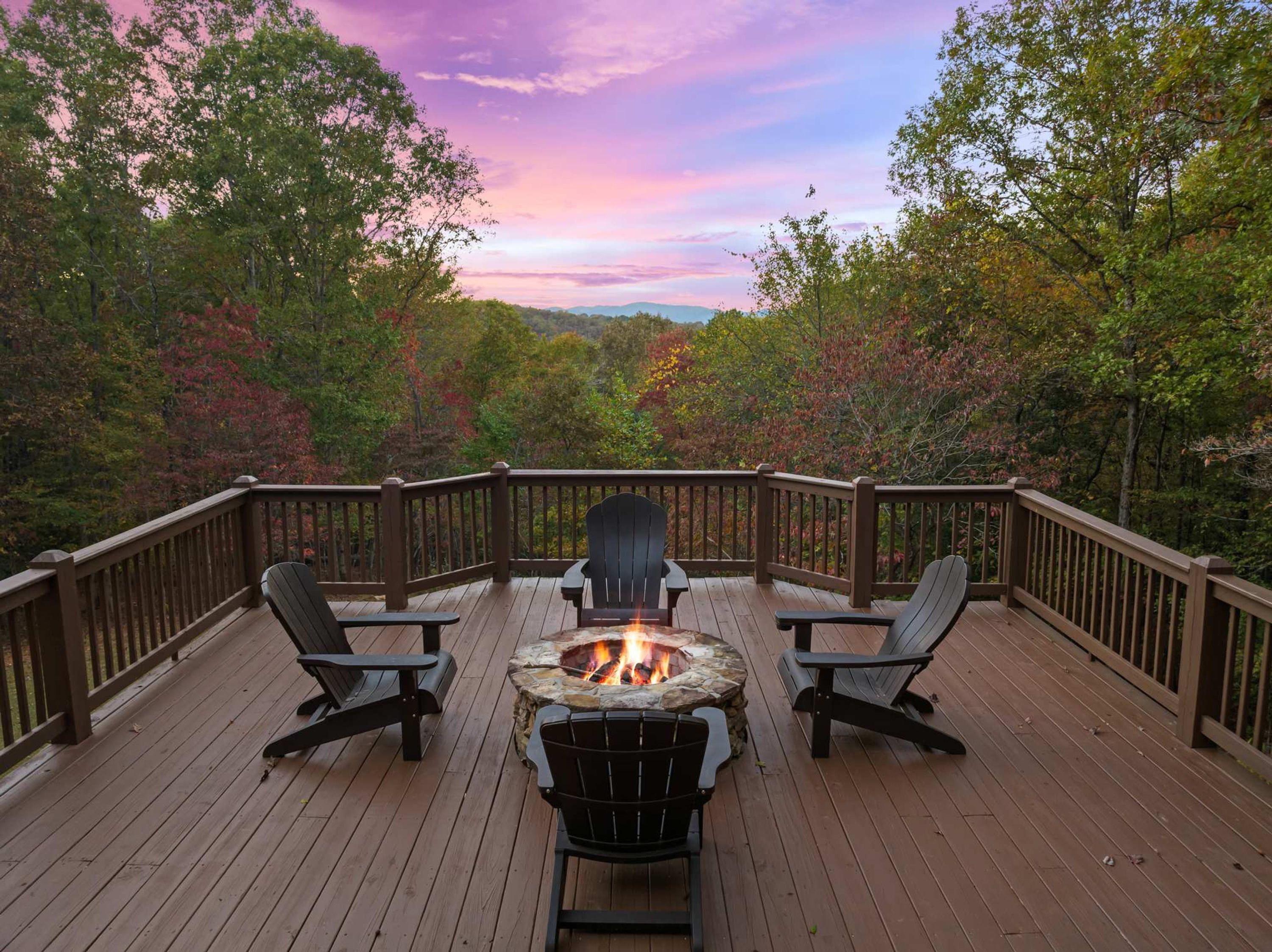A deck with a stone fire pit surrounded by chairs, overlooking a forested area.