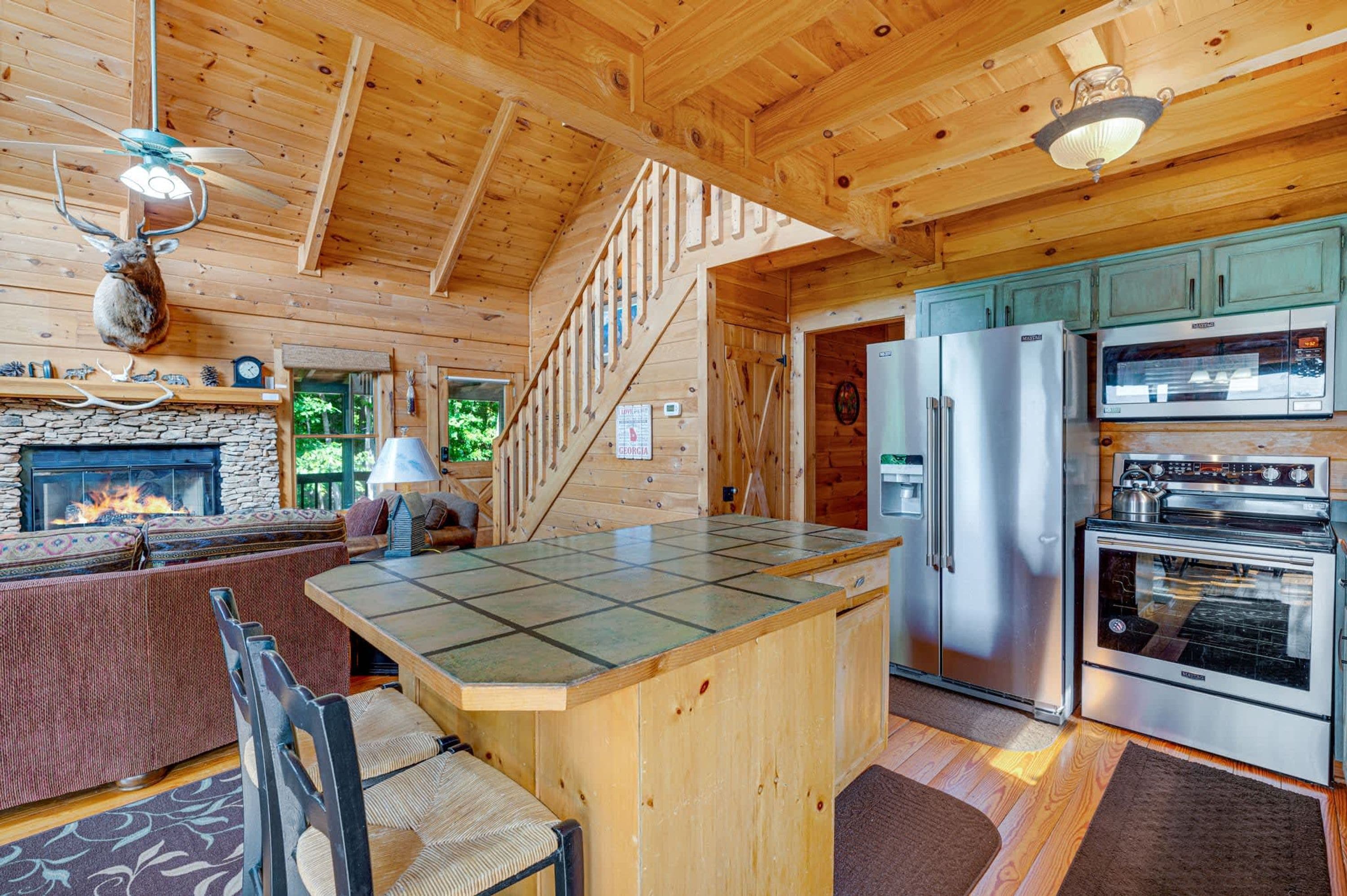 A cabin interior with a stone fireplace, a kitchen with stainless steel appliances, and a wooden dining area.