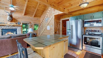 A cabin interior with a stone fireplace, a kitchen with stainless steel appliances, and a wooden dining area.